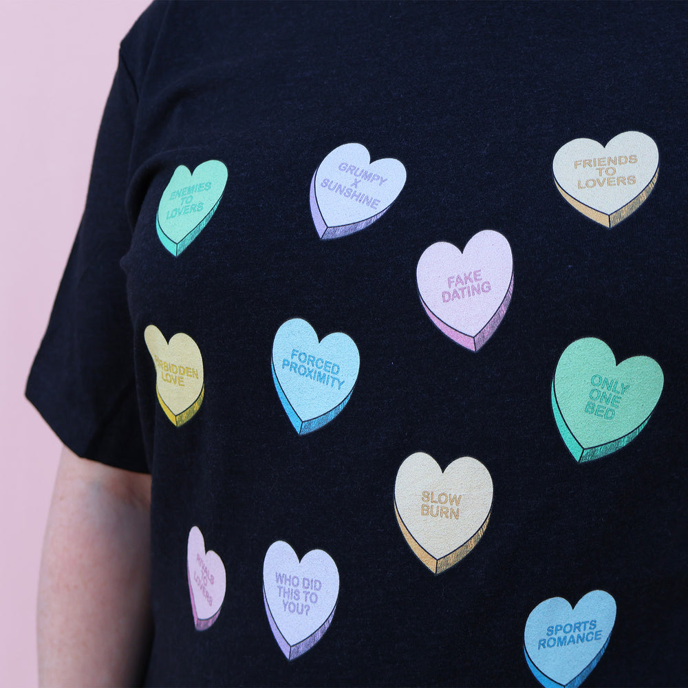 Black t-shirt with colorful heart-shaped trope designs on a pink background