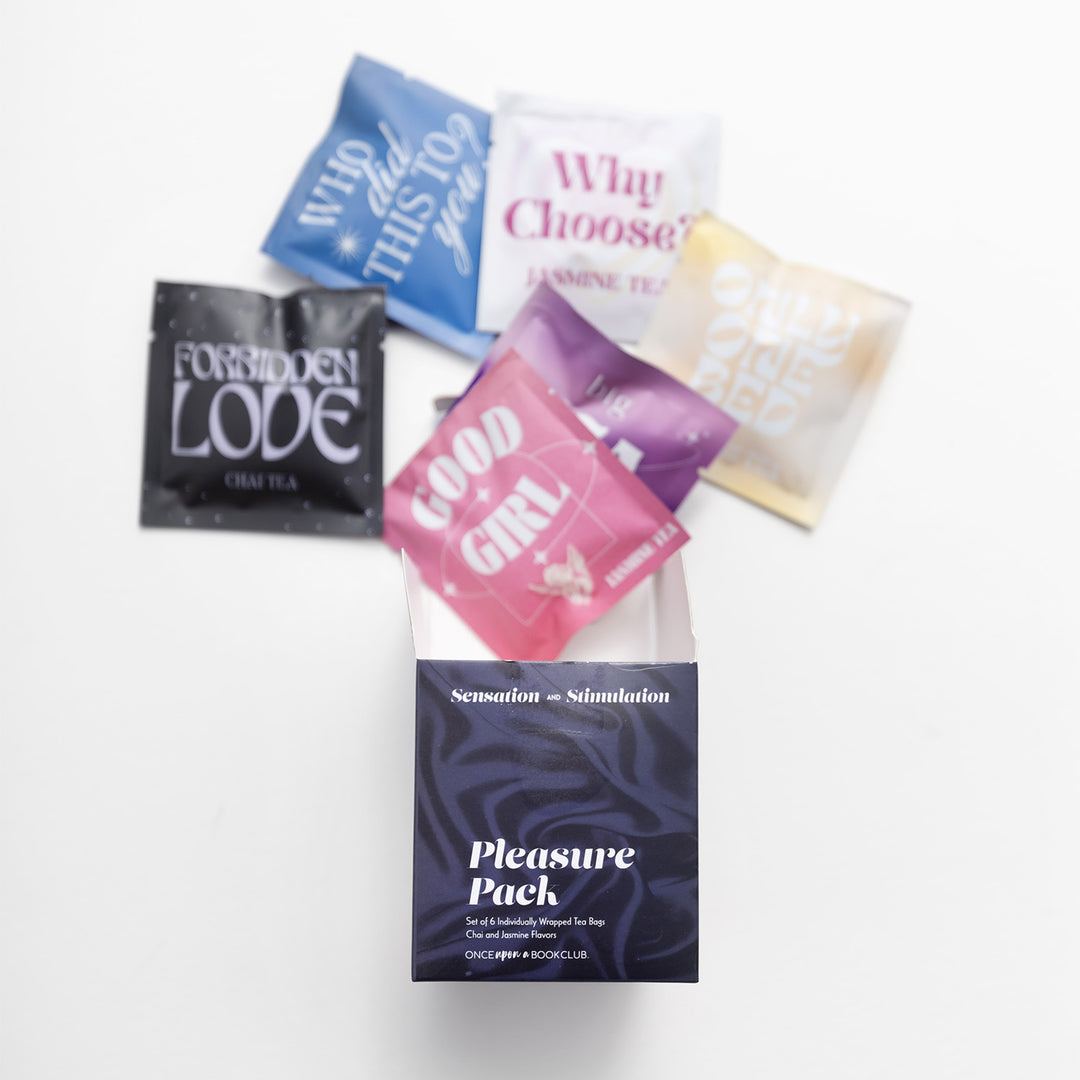 An open dark purple and black box labeled Pleasure Pack set of 6 individually wrapped tea bags, with 6 multicolored bags of tea spilling out. Each bag has a phrase: Forbidden Love, Who did this to you?, good girl, why choose?, only one bed, big Tea energy
