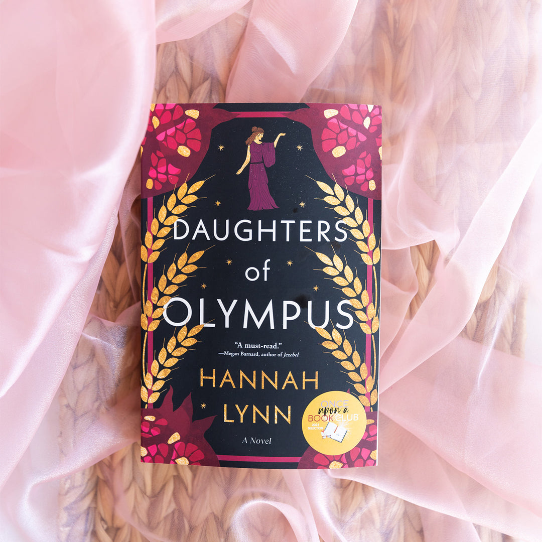 a paperback copy of Daughters of Olympus by Hannah Lynn sits on pink tulle.