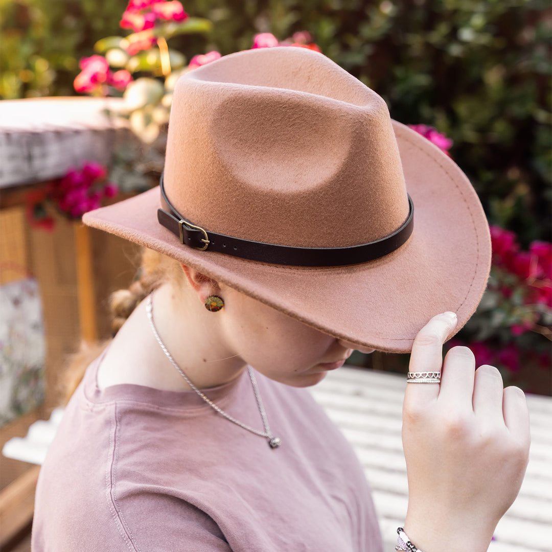 A woman pulls down on the brim of a brown cowboy hat with a dark brown strap.