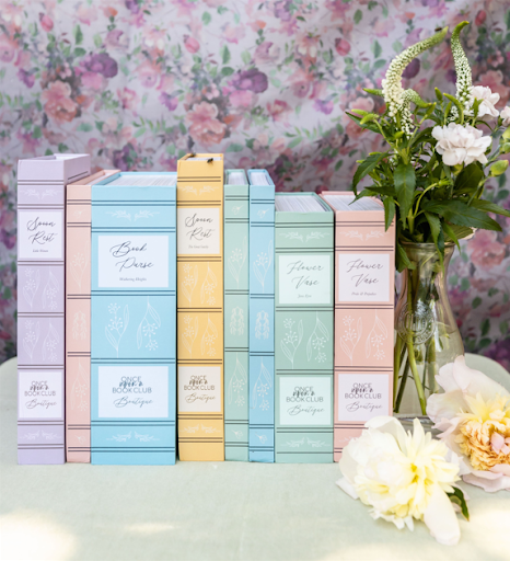 A collection of pastel-colored book spines arranged neatly, featuring titles from Once Upon a Book Club, alongside a vase of fresh flowers.