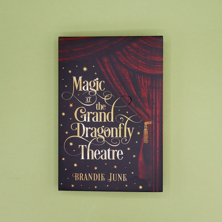 Book cover of 'Magic at the Grand Dragonfly Theatre' by Brandie June with red curtain design on a green background