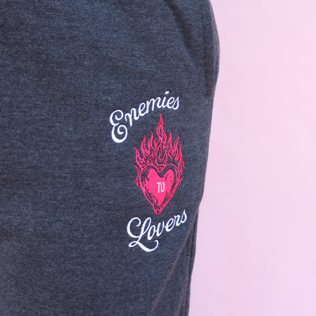 Embroidered design on a dark fabric with 'Enemies to Lovers' text and a heart with flames.
