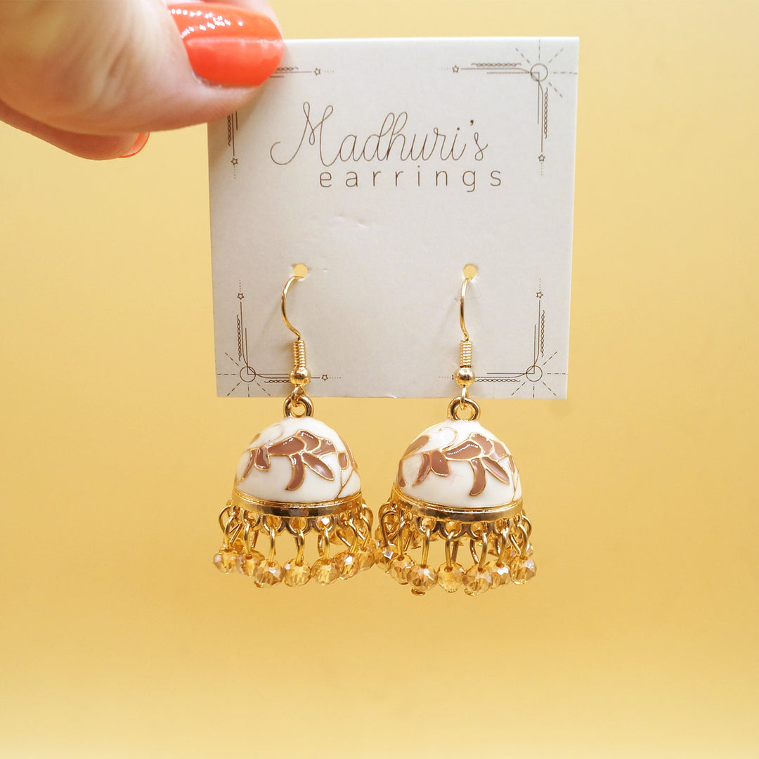 a white hand holds a pair of gold, white, and brown Jhumka Earrings 