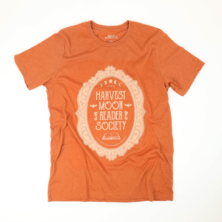 A heather-orange short-sleeve t-shirt with a cream-colored graphic on the front that reads 'Harvest Moon Reader Society' inside an ornate oval frame, laid flat on a white background.