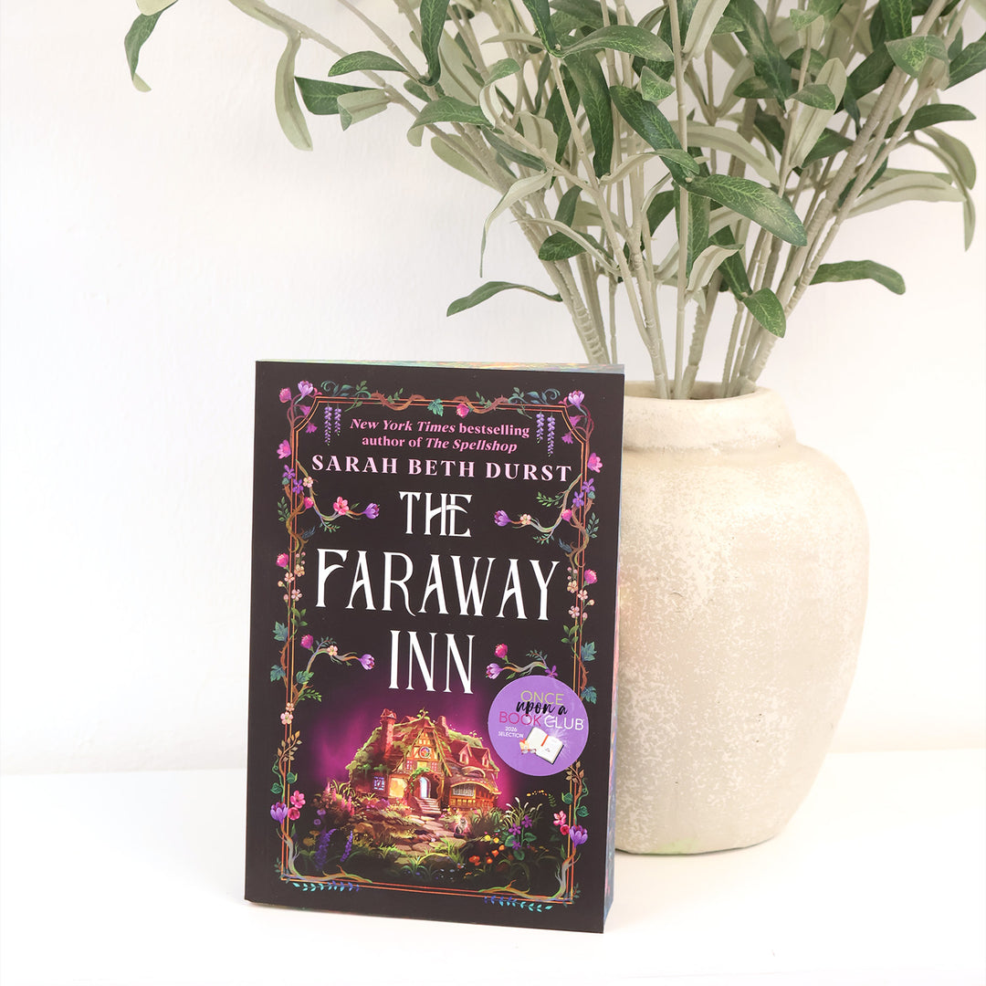 The Faraway Inn book by Sarah Beth Durst standing upright next to a large beige ceramic vase with green leaves, set against a clean white background.