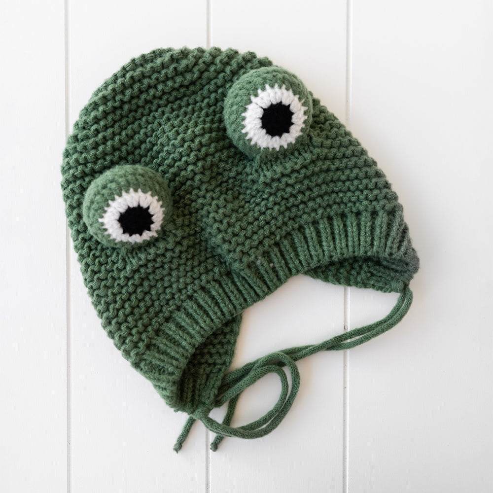 A dark green crochet hat that looks like a frog with eyes sticking out the top.