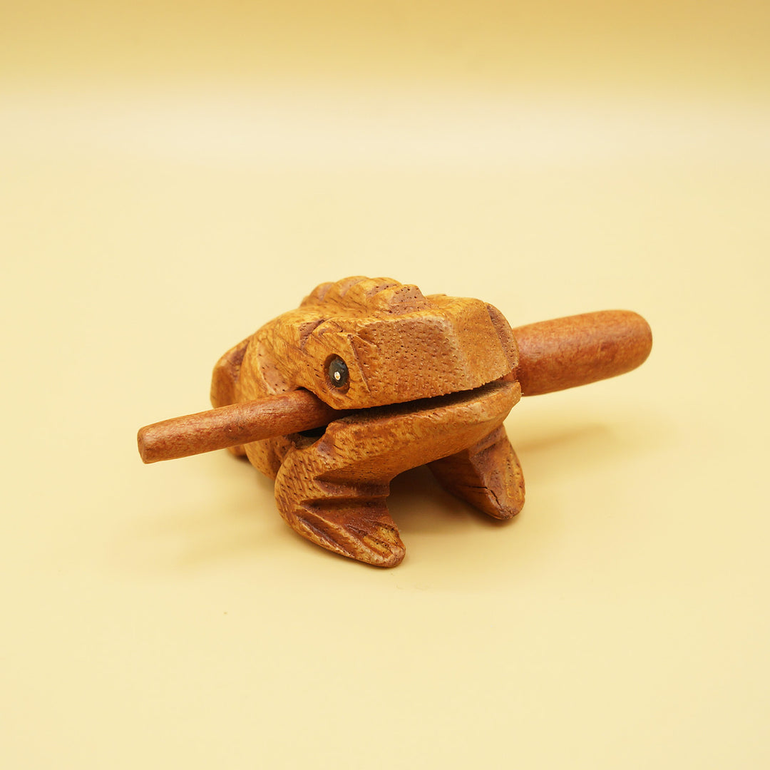 a wooden frog holding a wooden stick in its mouth