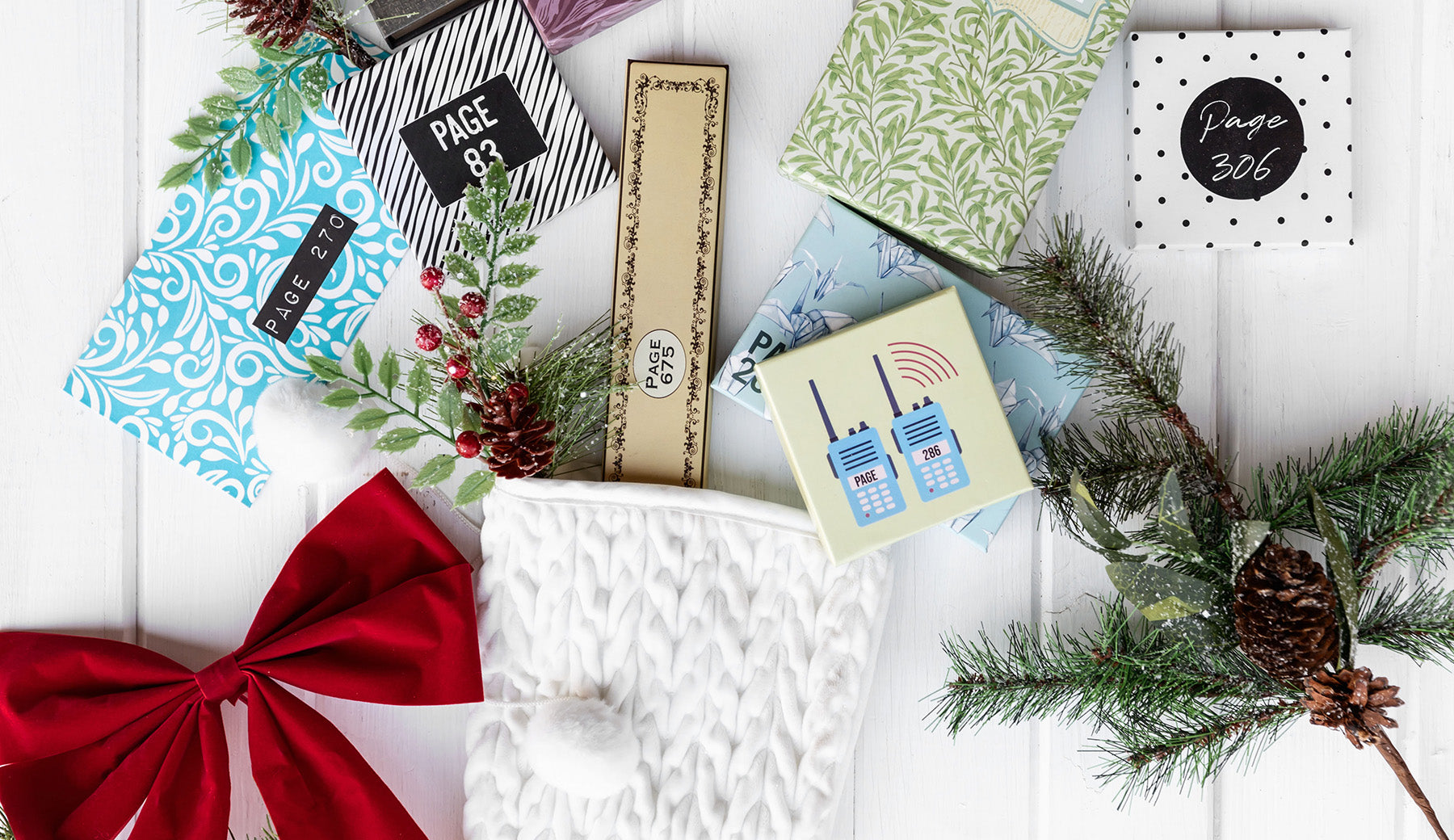 A collection of wrapped gifts labeled with page numbers are spread out above a white knit stocking, holiday greenery, and a red bow. 