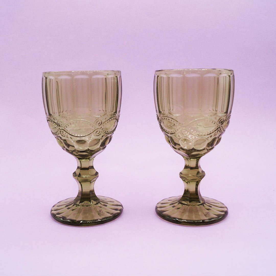 Two green, vintage-style glass goblets on a light purple background