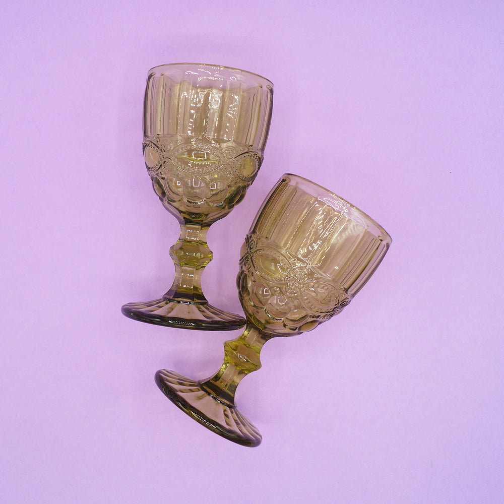 Two green, vintage-style glass goblets on a light purple background