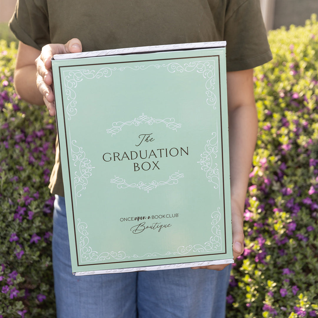 A white woman holds a closed Graduation box outdoors.