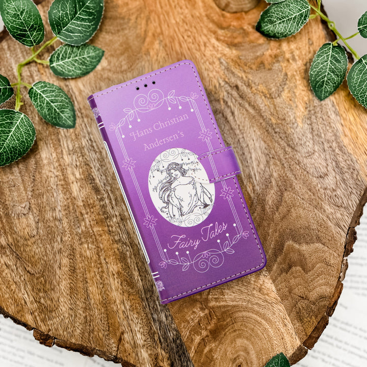 Hans Christian Andersen Fairy Tales phone case with fairy design on a wooden surface with leaves.
