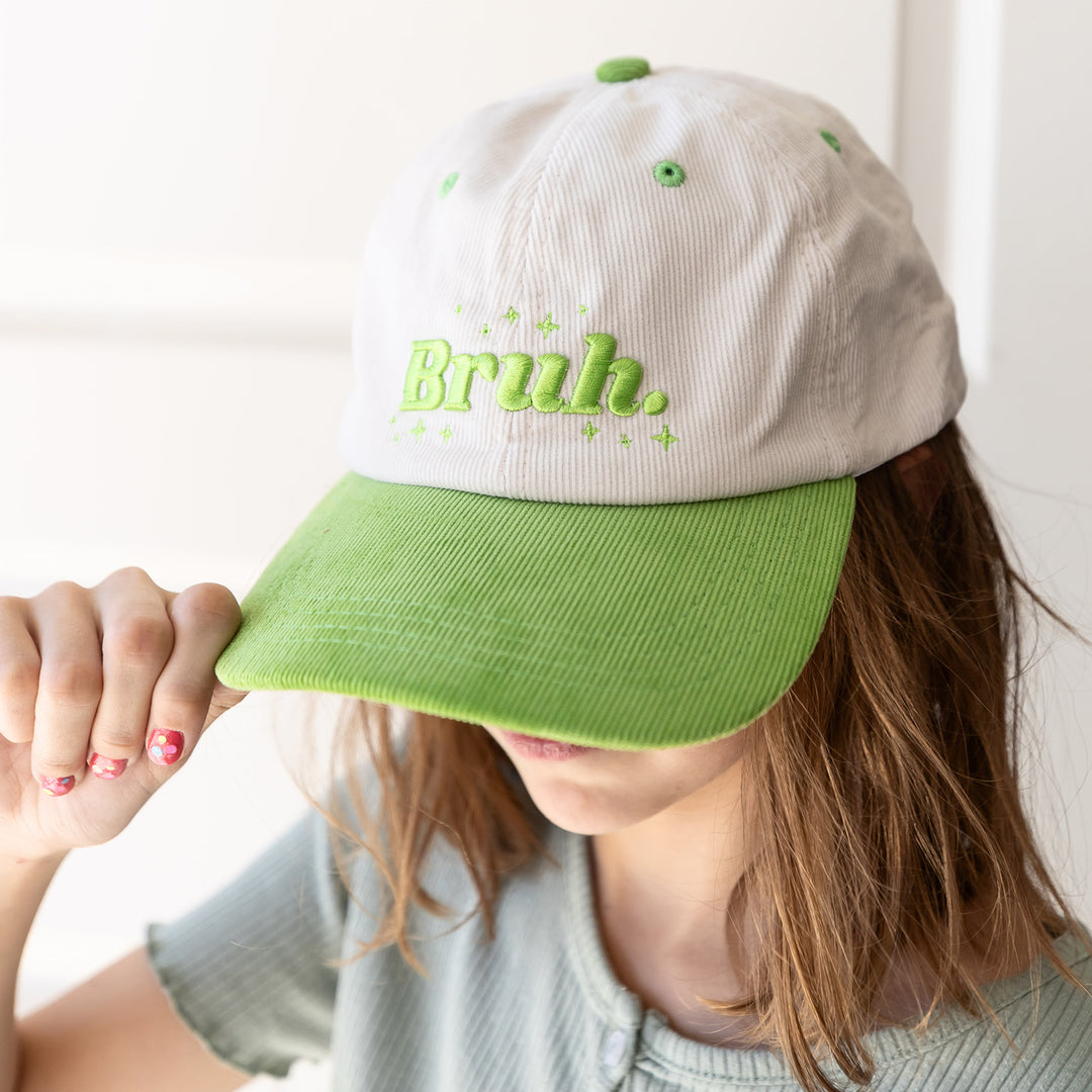 a cream and lime green corduroy hat with the word "Bruh" embroidered in lime green on the front along with lime green stars embroidered around it.