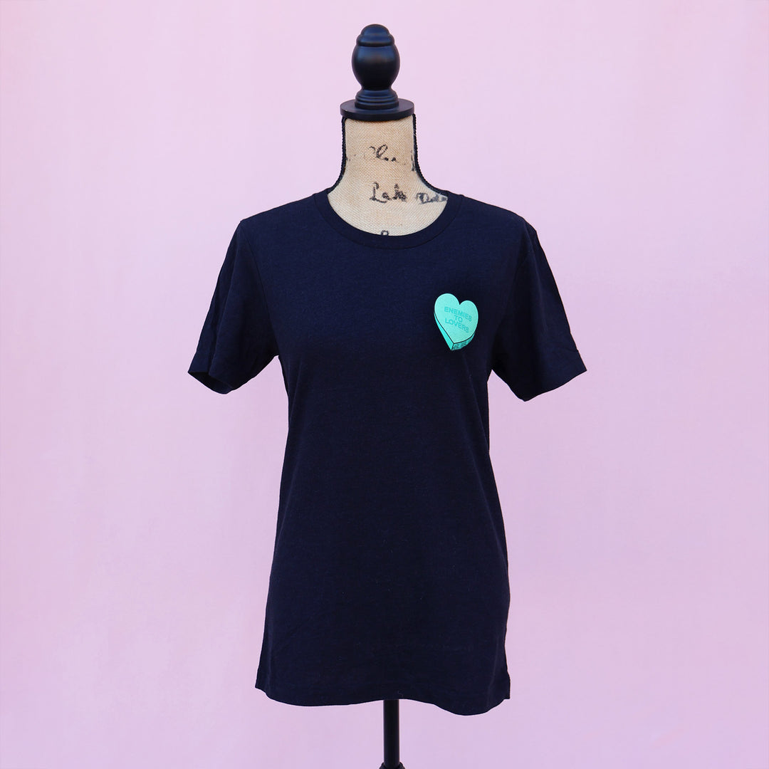 Black t-shirt with a green heart-shaped candy design and 'Enemies to Lovers' text on a pink background.