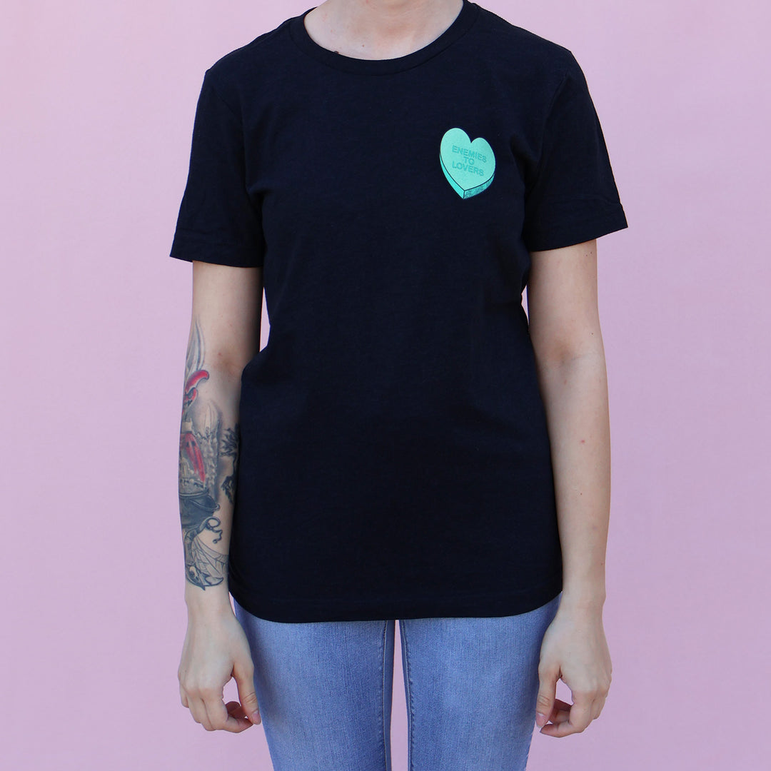 Black t-shirt with a green heart-shaped candy design and 'Enemies to Lovers' text on a pink background.