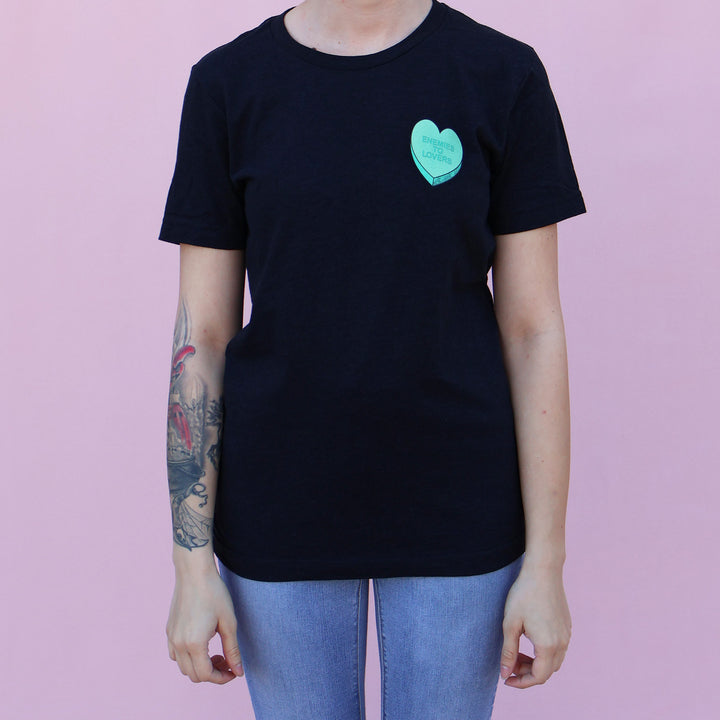 Black t-shirt with a green heart-shaped candy design and 'Enemies to Lovers' text on a pink background.