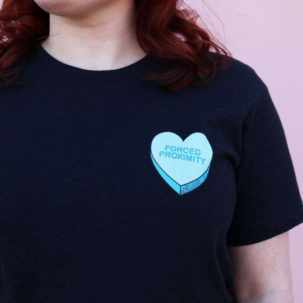 Black t-shirt with a blue heart-shaped candy design and 'Forced Proximity' text on a pink background.