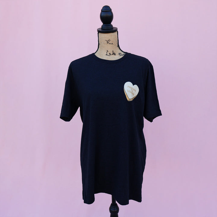 Black t-shirt with an orange heart-shaped candy design and 'Friends to Lovers' text on a pink background.