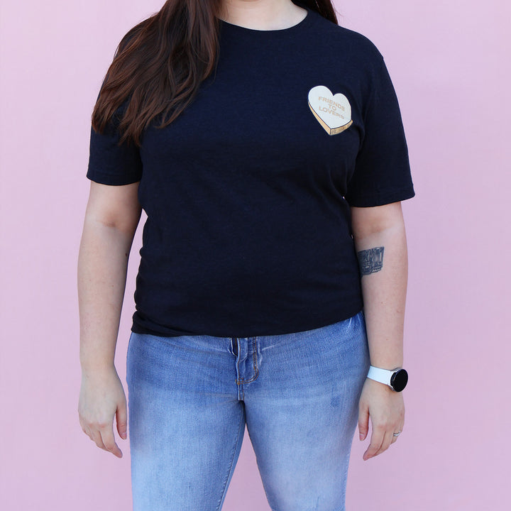 Black t-shirt with an orange heart-shaped candy design and 'Friends to Lovers' text on a pink background.
