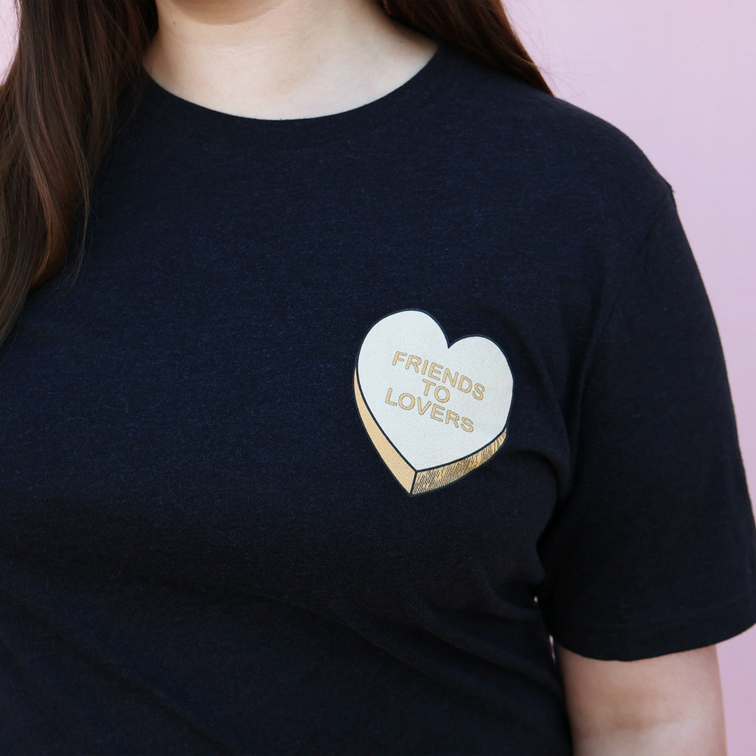 Black t-shirt with an orange heart-shaped candy design and 'Friends to Lovers' text on a pink background.