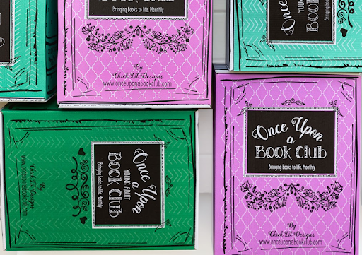 A close-up of colorful Once Upon a Book Club boxes in green and pink, featuring the logo and the phrase "Bringing books to life. Monthly."