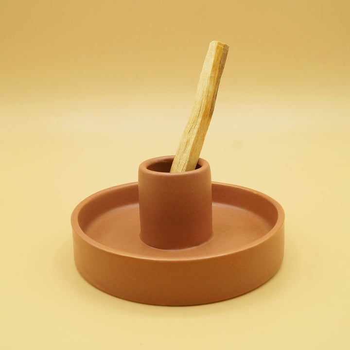 a round, clay colored dish with a 2" center piece holding the piece of palo santo wood.