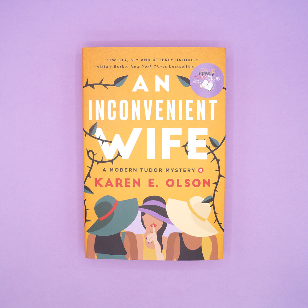 a hardcover copy of AN INCONVENIENT WIFE by Karen E. Olson on a purple background.