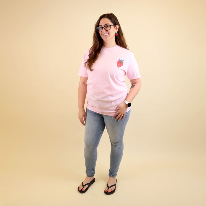 Woman wearing a pink t-shirt with a strawberry designs and text that says 'Reading is my Jam' on a beige background