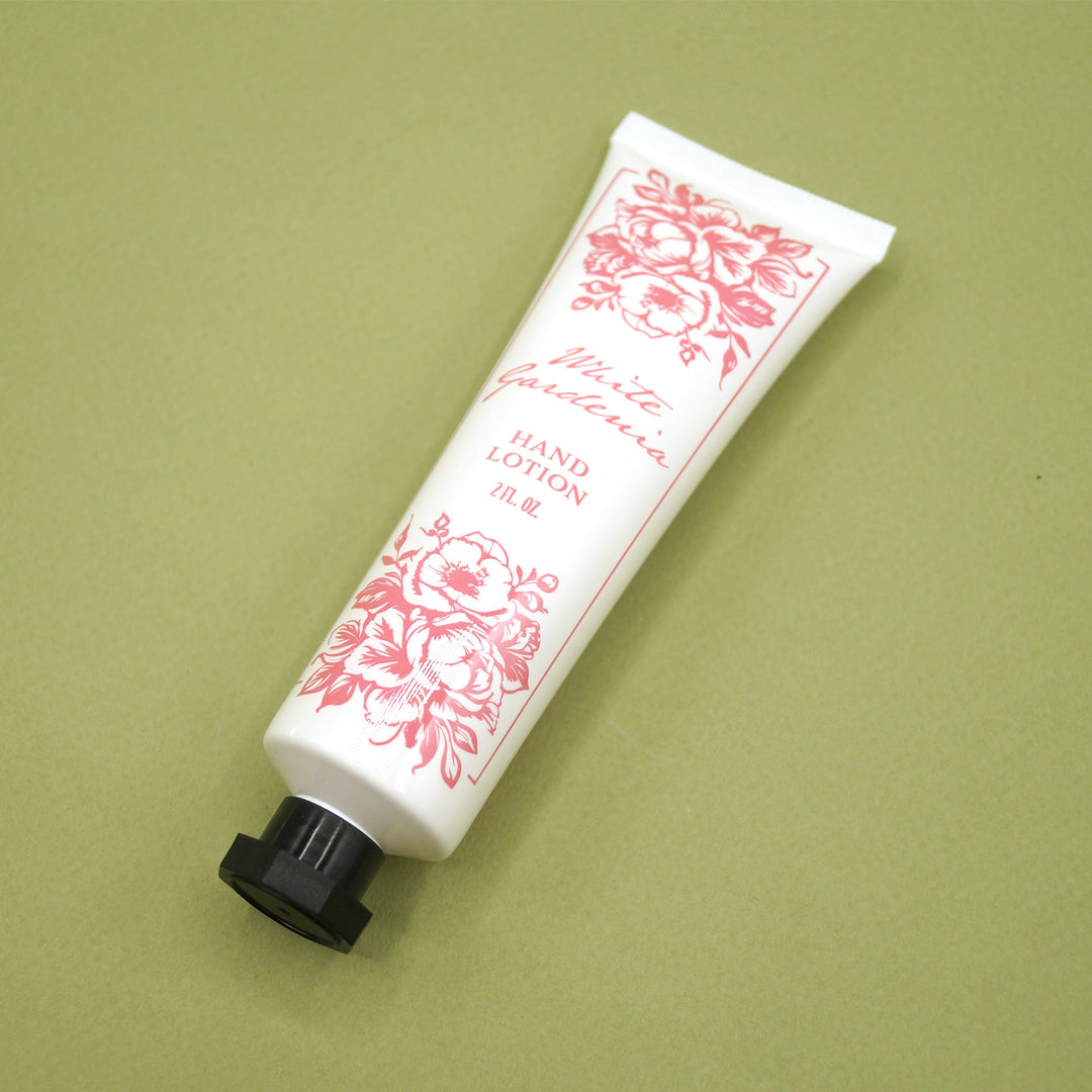 A white hand lotion bottle with a black cap. There are pink flowers and lettering on the front: White Gardenia - Hand Lotion 2 fl oz.