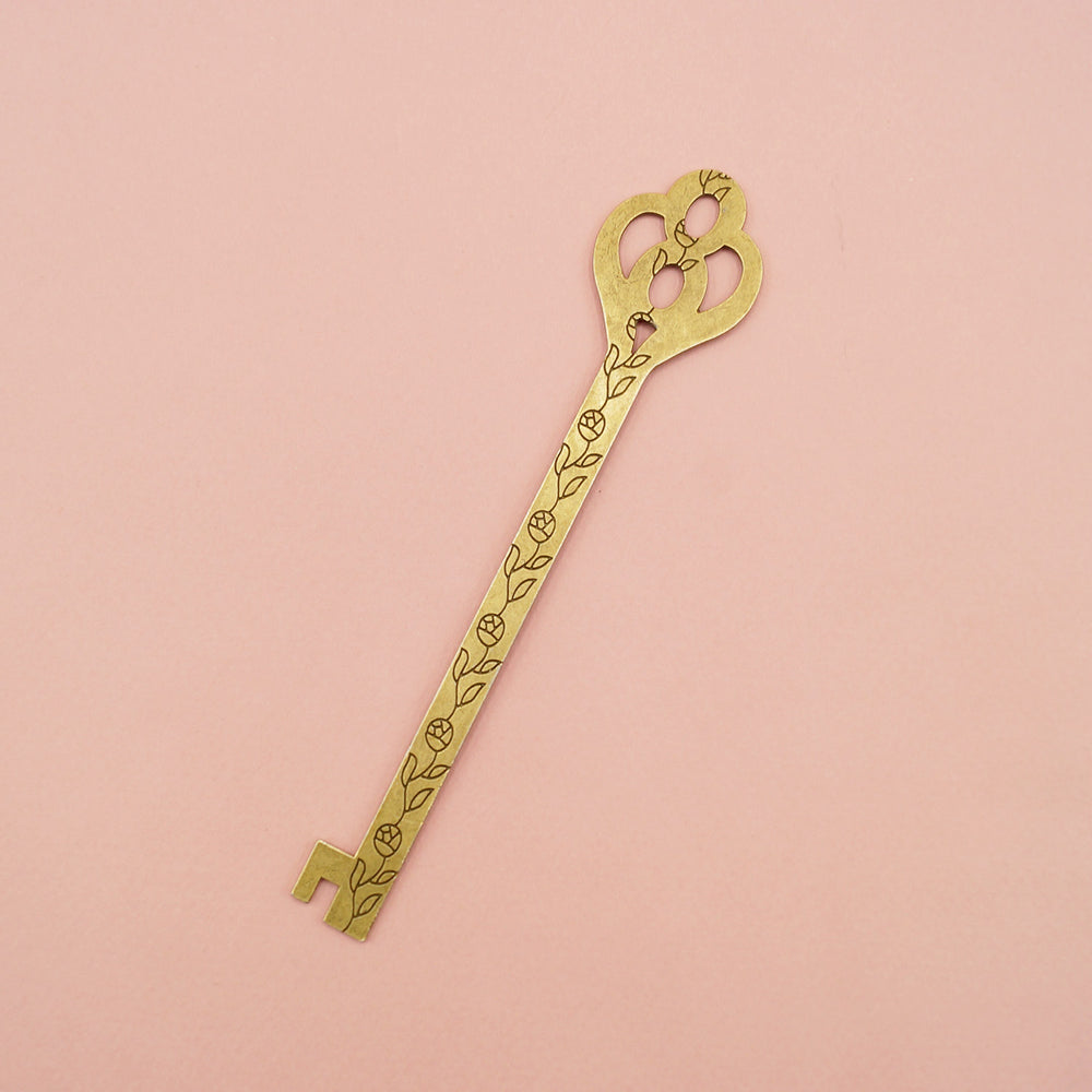 A gold metal key-shaped bookmark with a black flower pattern down the center