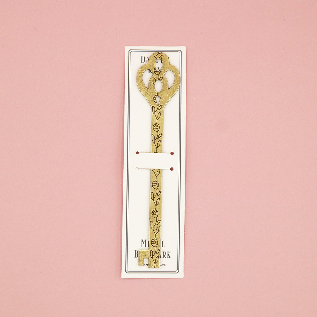 A gold metal key-shaped bookmark with a black flower pattern down the center