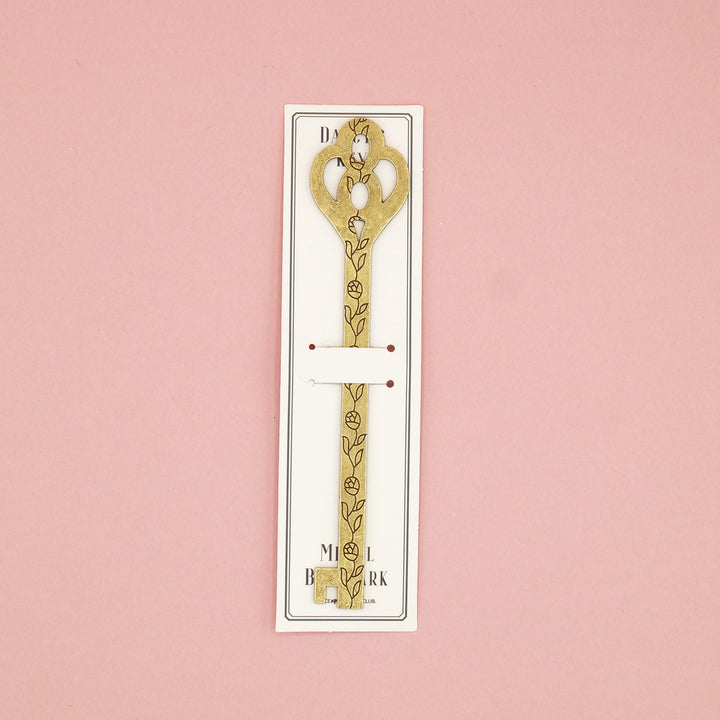 A gold metal key-shaped bookmark with a black flower pattern down the center