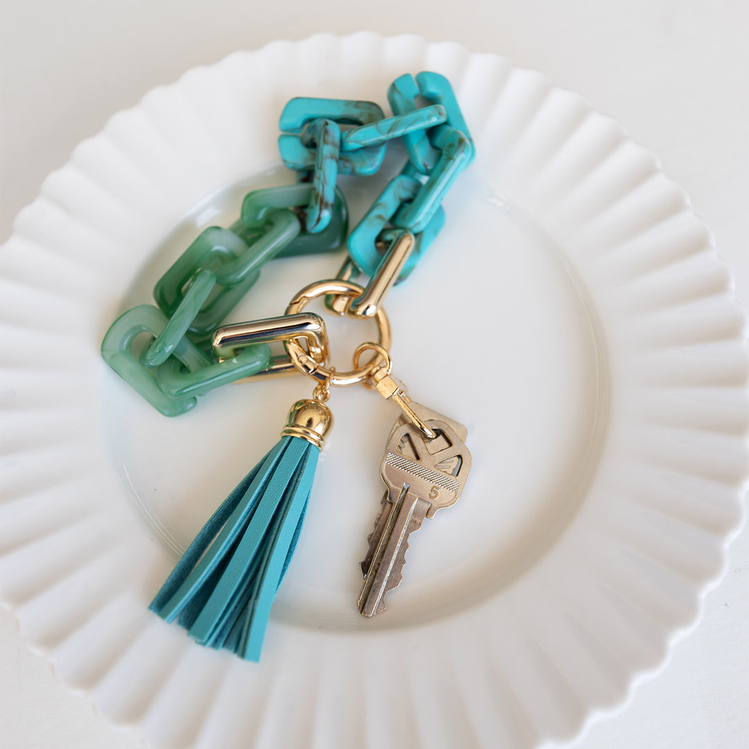 A key ring with two keys, a blue tassle, and a blue ombre circular chain.