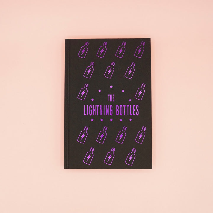 the custom black fabric hardcase of The Lightning Bottles by Marissa Stapley showcasing the shiny purple foiling featuring lightning bolts inside bottles and the book title.