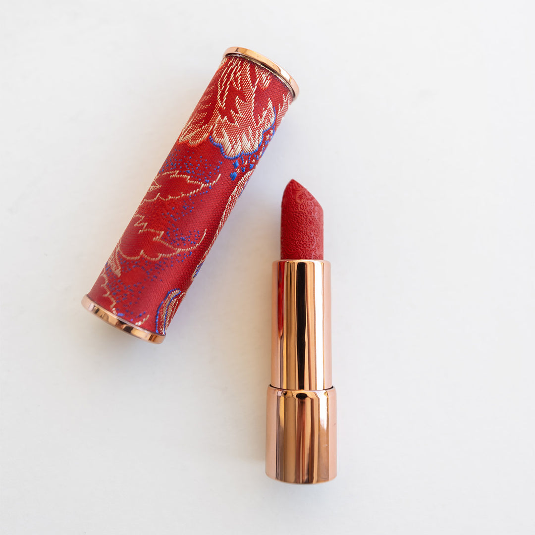 A gold tube of red lipstick. The red lipstick has a lace pattern and the cover for the lipstick is red and gold.