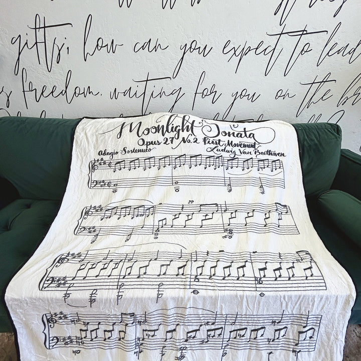 A white fleece blanket featuring Beethoven's Moonlight Sonata lays across a green couch