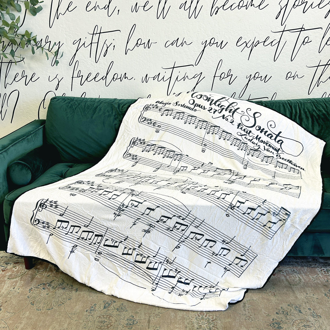 A white fleece blanket featuring Beethoven's Moonlight Sonata lays across a green couch