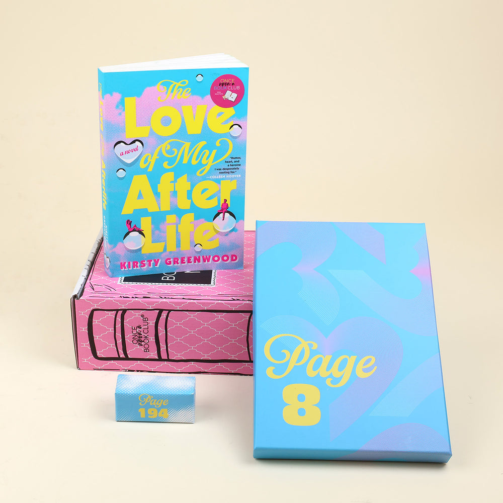 The Magical Realism Mini box items featuring the book 'Love of my Afterlife' by Kirsty Greenwood, a blue wrapped gift labeled 'PAGE 8', and a small blue and white gift with text reading 'PAGE 194', arranged on a beige background.