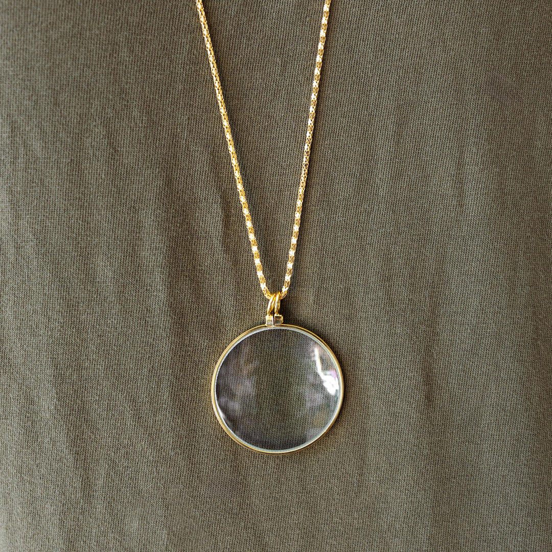 A gold necklace with a magnifying glass, laying on a green background.