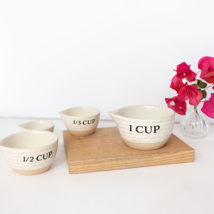 a set of ceramic measuring cups featuring a subtle script writing design including 1/4, 1/3, 1/2, and 1 cup.