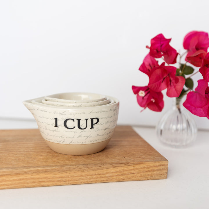 a set of ceramic measuring cups featuring a subtle script writing design stacked within each other.