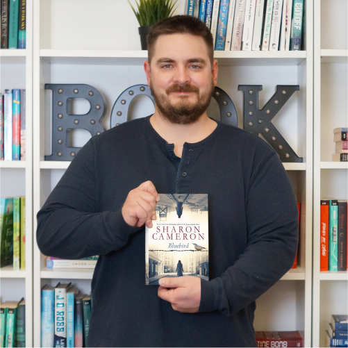 A man wearing a navy blue shirt smiles while holding the book 