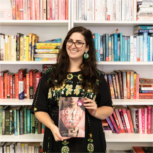 A woman wearing a black dress with floral details smiles while holding the book 