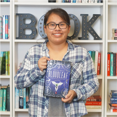 A woman wearing a plaid shirt smiles while holding the book 