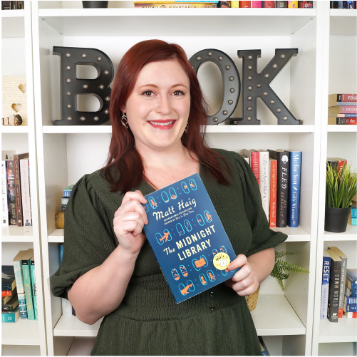 A woman wearing a green dress smiles while holding the book 