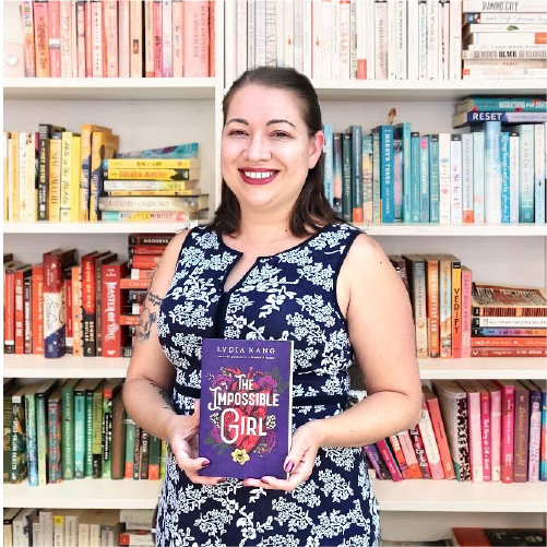 A woman wearing a floral navy blue dress smiles while holding the book 