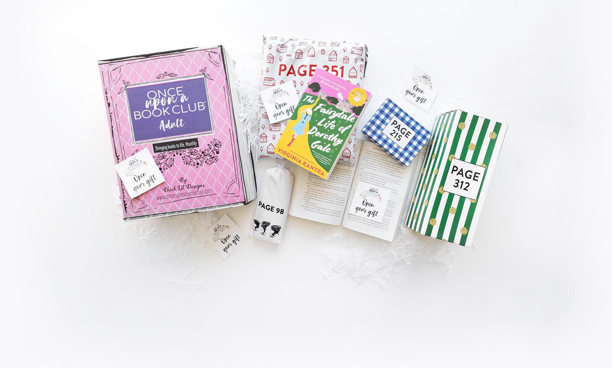 A pink Once Upon a Book Club box sits next to an open book. The book has an 'open your gift' sticky note on the page. Wrapped gifts labeled with page numbers and many other open your gift sticky notes surround the open book emphasizing that you open the gifts as you read!