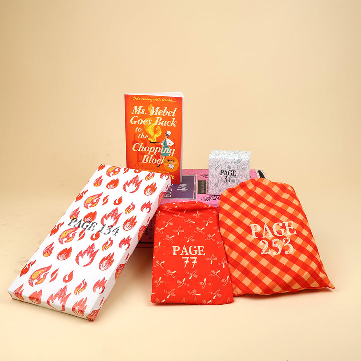 A new copy of Ms. Mebel Goes Back to the Chopping Block by Jesse Q. Sutanto sits on a pink OUABC box. Also pictured are four wrapped gifts labeled with page numbers to open as you read!