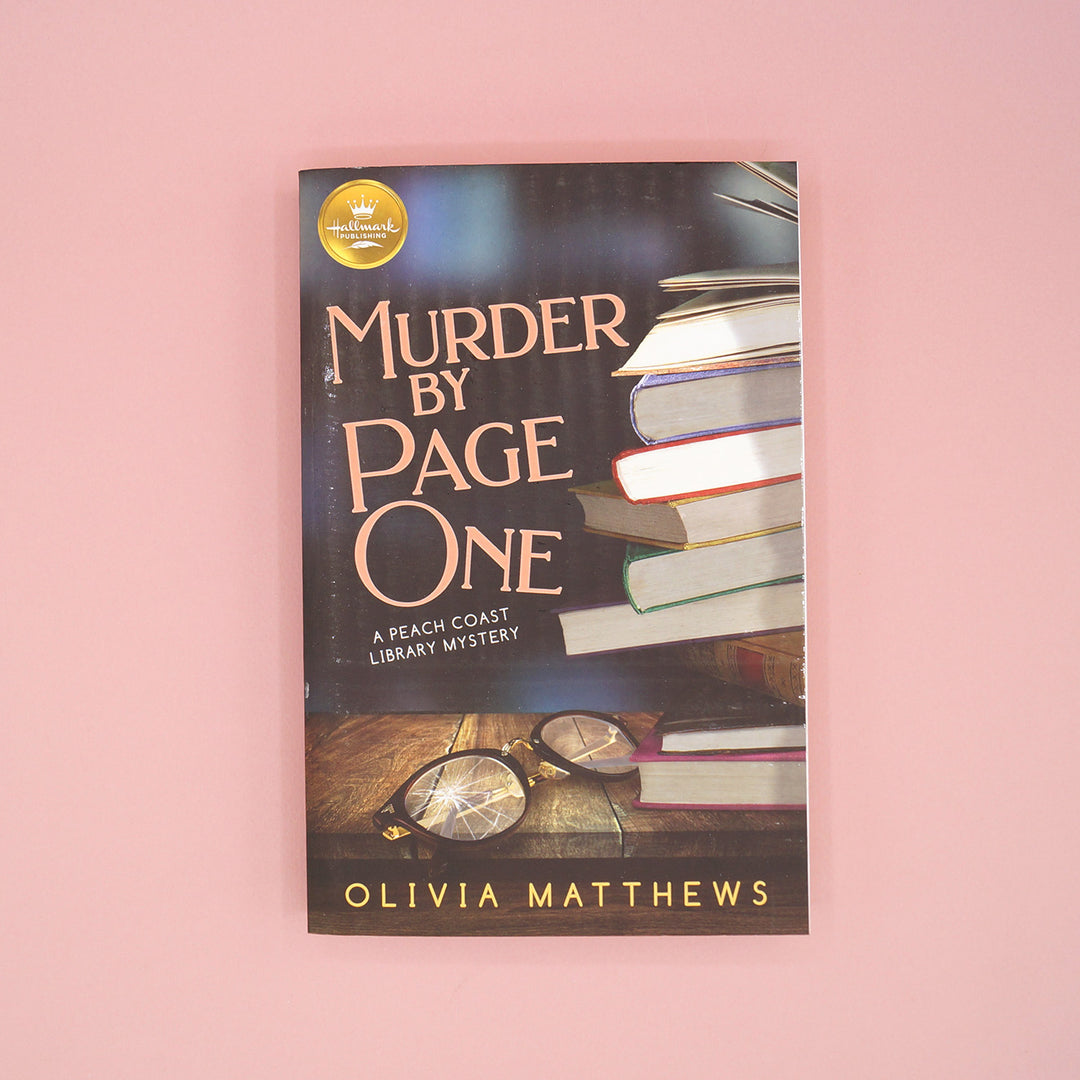 A paperback copy of Murder by Page One by Olivia Matthews sits on a pink background.